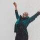 woman in green jacket raising her hands