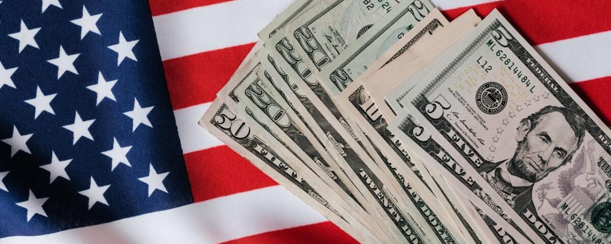 American flag background. on top of the flag is US currency in various denominations.
