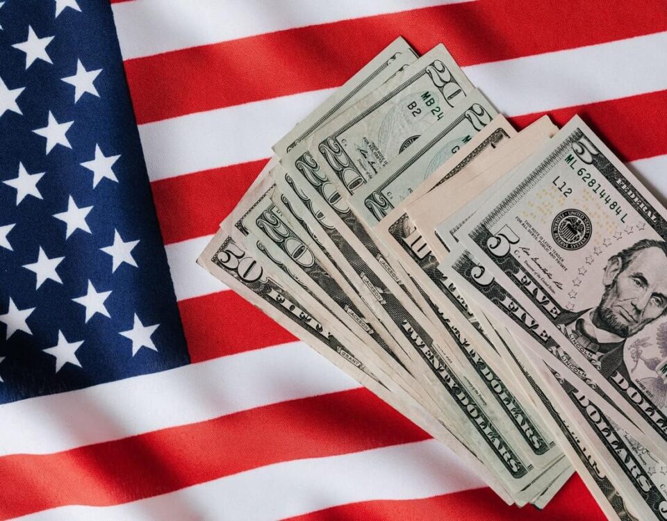 American flag background. on top of the flag is US currency in various denominations.