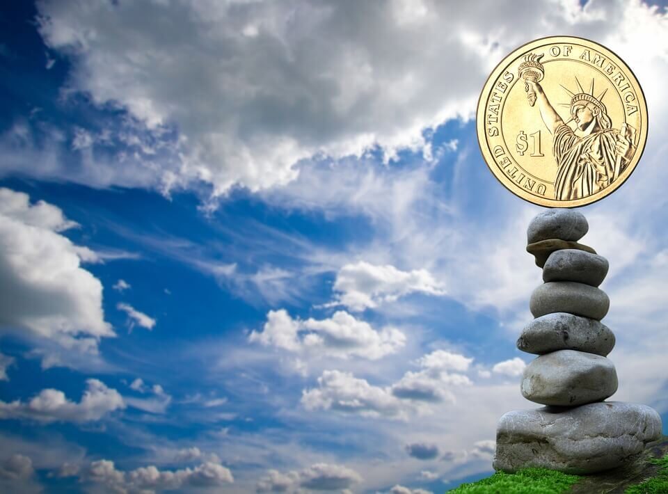 blue sky with fluffy white clouds. On the right is a stack of 7 river rocks stacked atop one another. At the top is a US gold $1 coin with the Statue of Liberty on it.