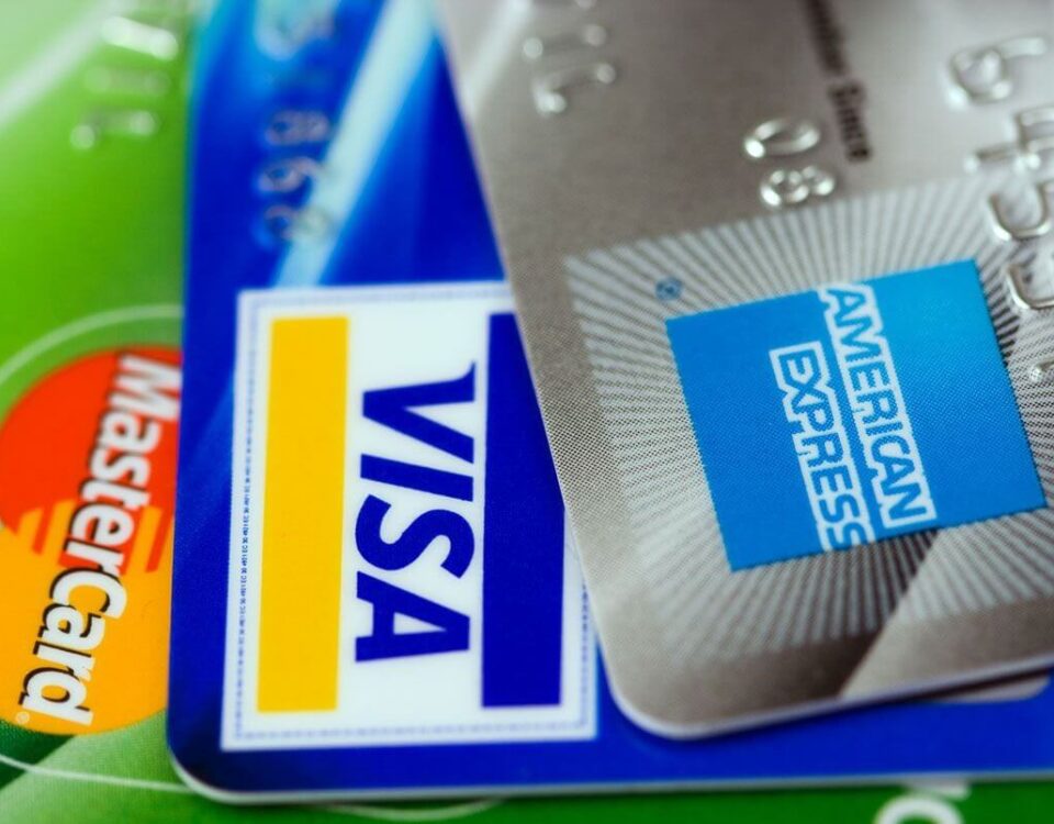 on the left is a bright green Mastercard with logo, the center is a blue visa card, and the card on the right is a gray card with blue American express logo
