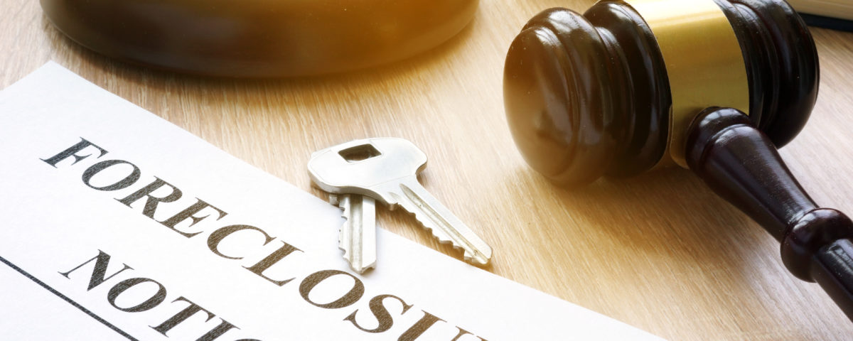 brown and gold gavel lying on a desk with gavel rest. 2 silver keys laying near a foreclosure notice