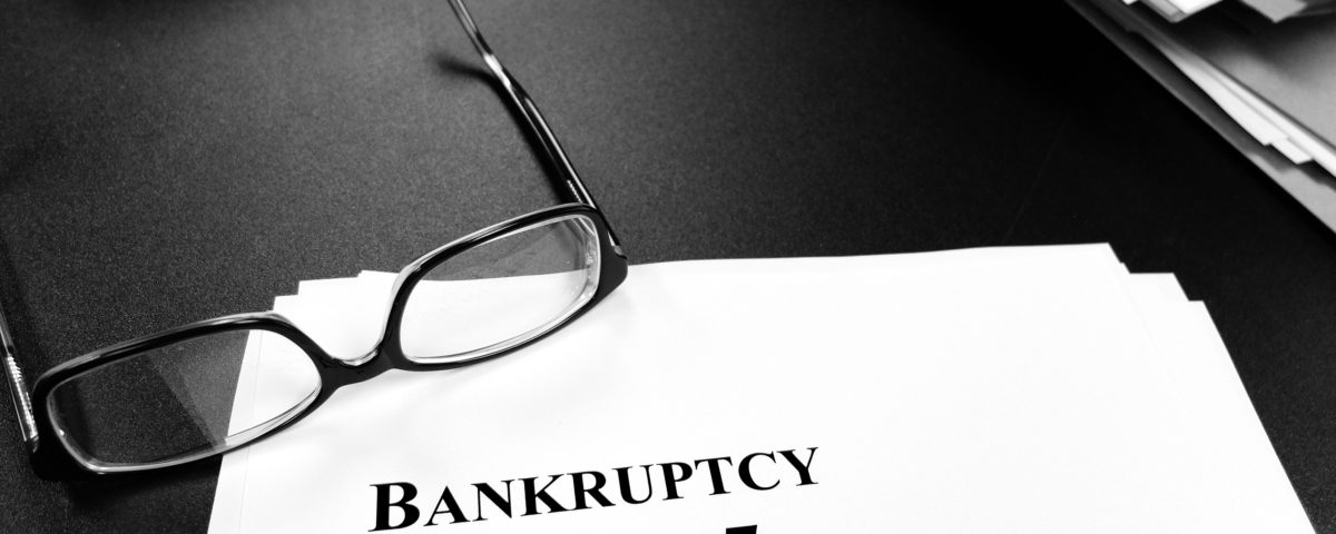 black and white image of file folders on a desk, a pair of glasses laying on a sheet of paper that reads "Bankruptcy Chapter 7"