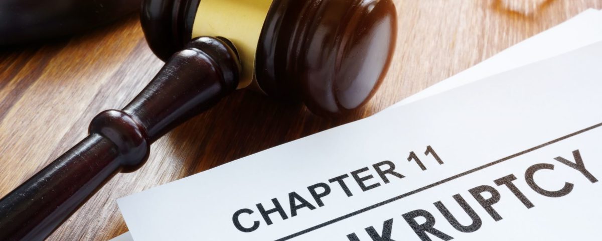 dark brown and gold gavel lying next to a chapter 11 bankruptcy filing paper on a wooden desk.