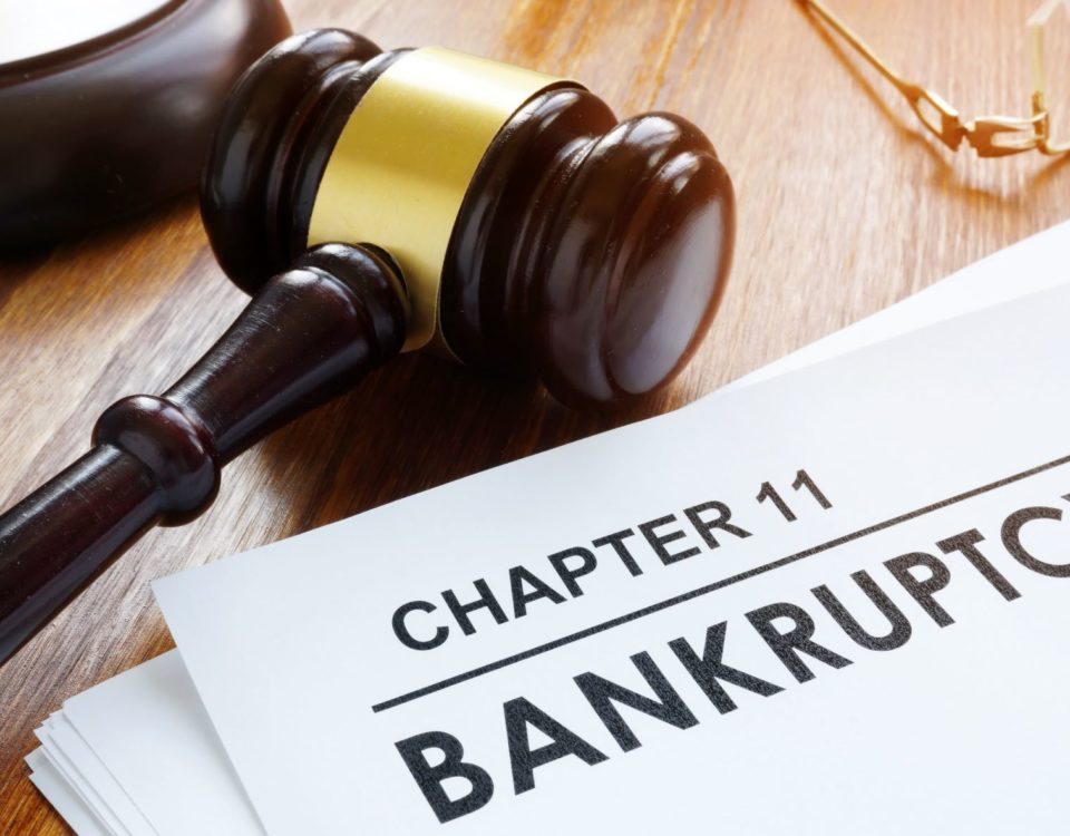 dark brown and gold gavel lying next to a chapter 11 bankruptcy filing paper on a wooden desk.