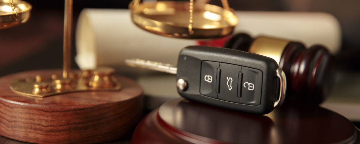 justice scales, brown and gold gavel in background with a car key fob sitting on a wooden gavel rest.