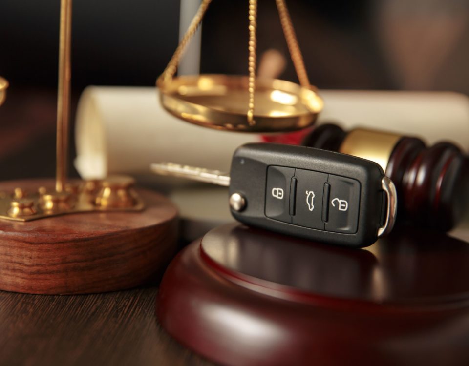 justice scales, brown and gold gavel in background with a car key fob sitting on a wooden gavel rest.