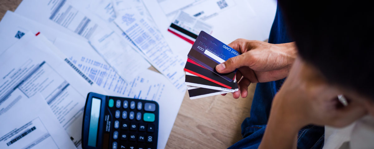 papers scattered on a floor with a calculator, person sitting on floor holding 4 credit cards