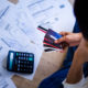 papers scattered on a floor with a calculator, person sitting on floor holding 4 credit cards