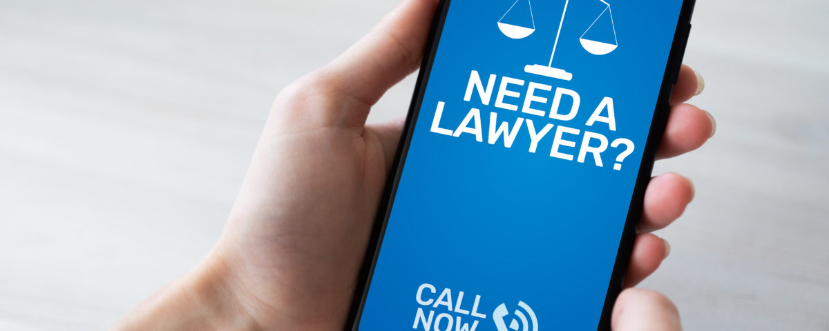 Hand holding a cell phone. On the screen, blue with white writing that says "Need a lawyer, call now"