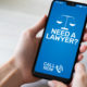 Hand holding a cell phone. On the screen, blue with white writing that says "Need a lawyer, call now"