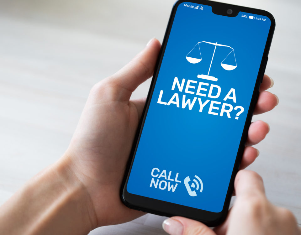 Hand holding a cell phone. On the screen, blue with white writing that says "Need a lawyer, call now"